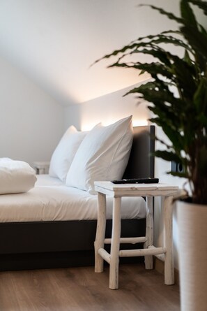 Un dormitorio moderno con cama, mesita de noche, televisor y planta en maceta.
