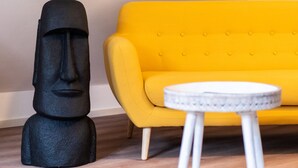 Una habitación con un sofá amarillo, una mesita blanca y una estatua negra.