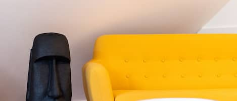 Una habitación con un sofá amarillo, una mesita blanca y una estatua negra.