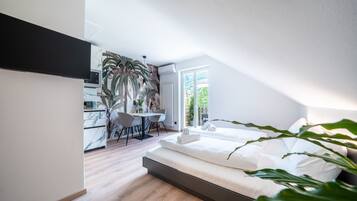 A modern bedroom with a large bed, a dining area with a table and chairs, and a kitchen area with a refrigerator and a microwave.