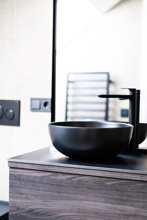 Une salle de bain moderne avec un meuble-lavabo en bois foncé, un lavabo noir et un robinet.