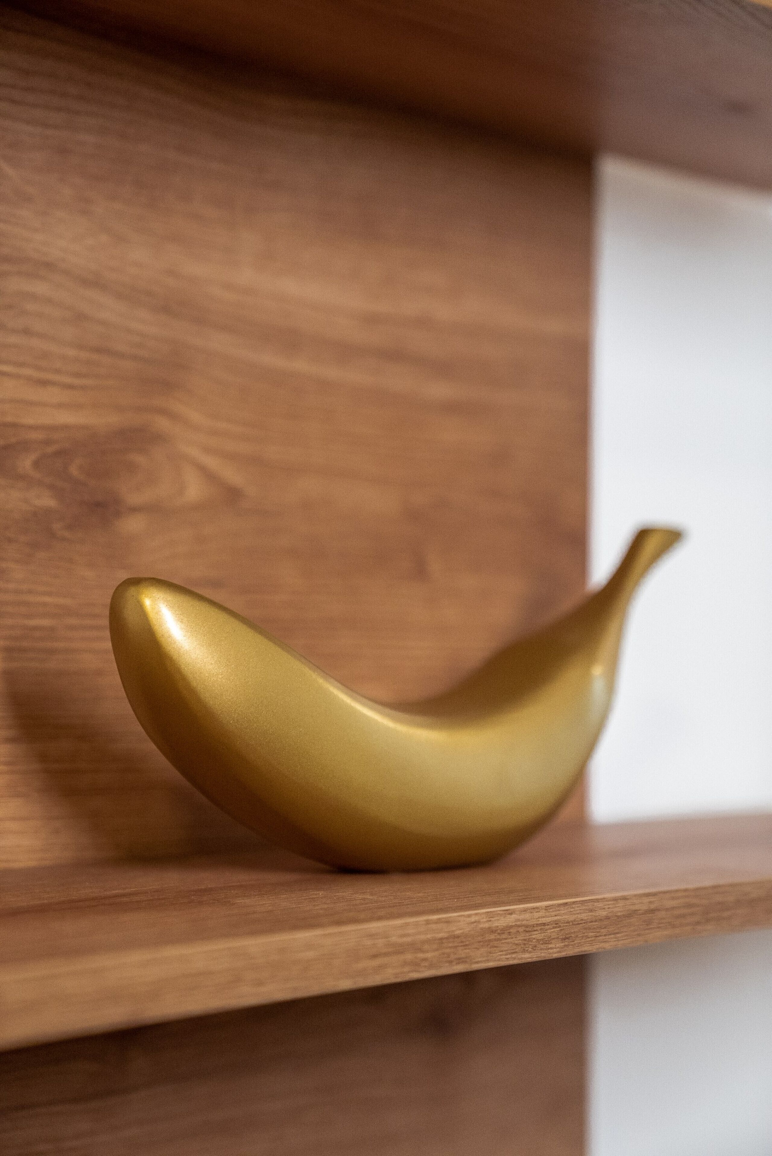 En hylla av trä med ett guldfärgat, bananformat föremål på.