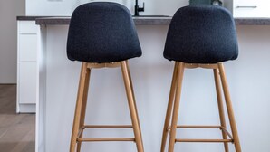 Une cuisine moderne avec deux tabourets de bar, des pieds en bois et un comptoir blanc.