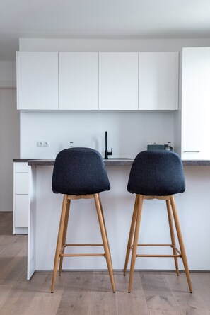 Een moderne keuken met twee barkrukken, houten poten en een wit aanrecht.