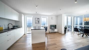 A modern kitchen with white cabinetry, a central island, and a dining area with a TV and seating.