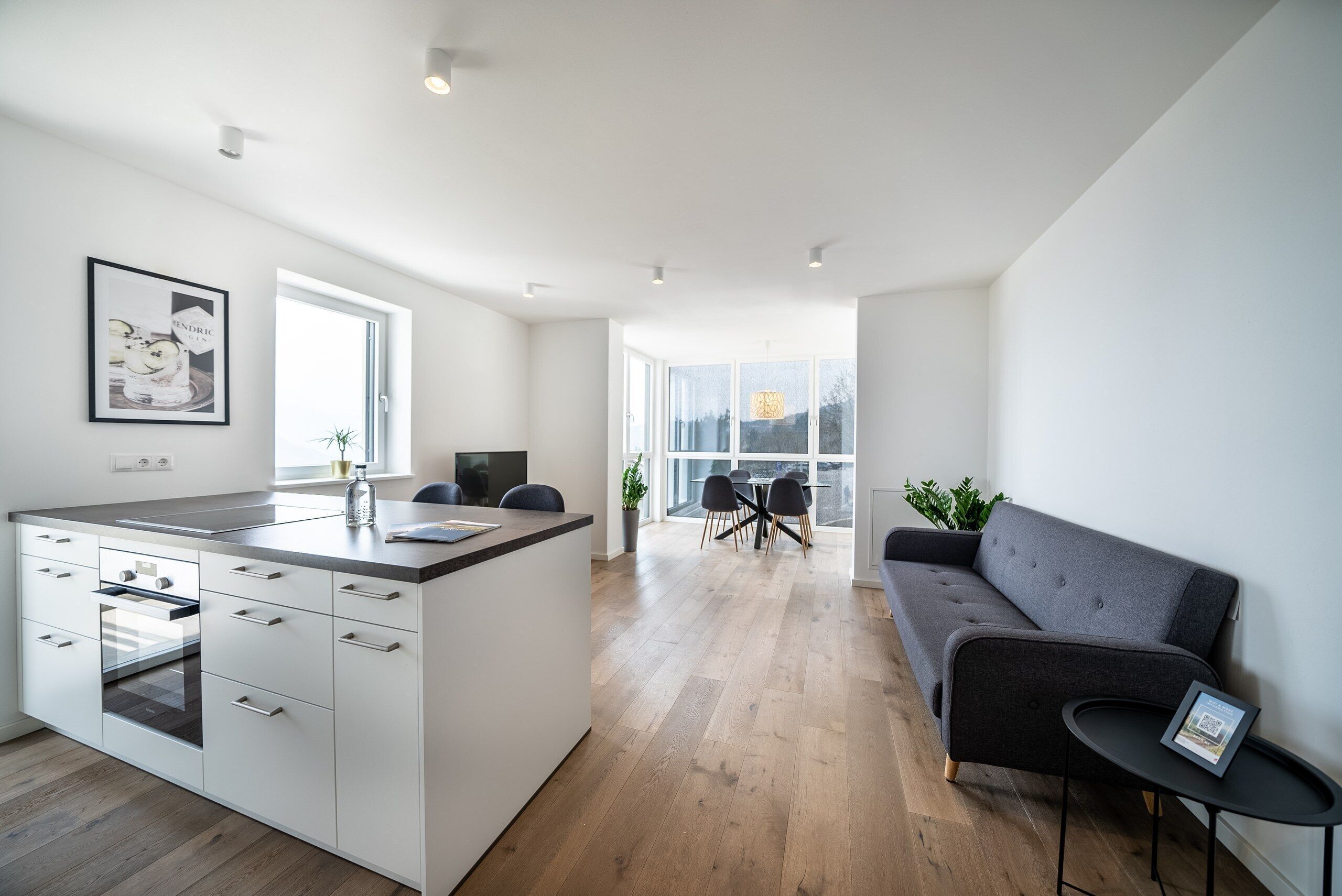 A modern kitchen with a central island, a dining area with a table and chairs, and a grey sofa.