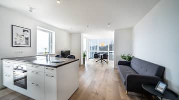 A modern kitchen with a central island, a dining area with a table and chairs, and a grey sofa.