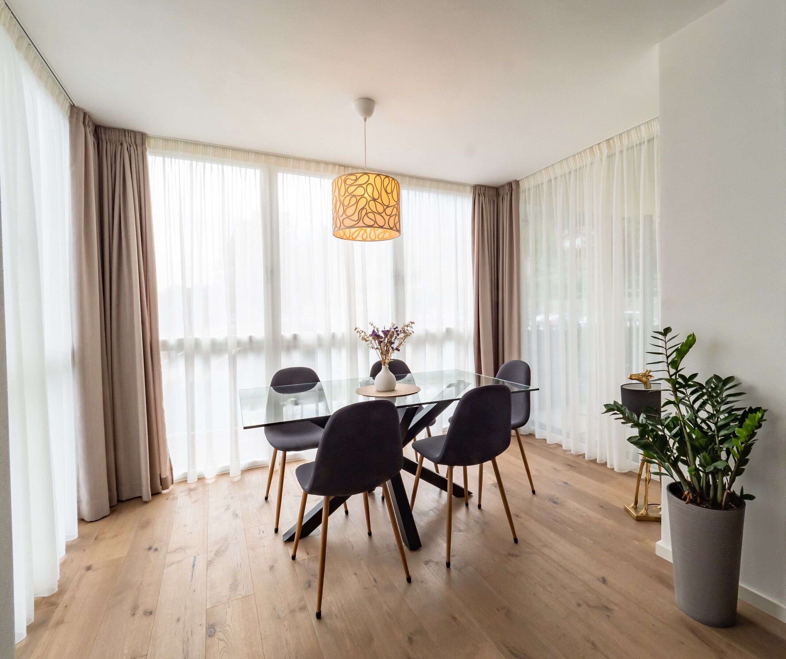 A dining area with a glass table, black chairs, a vase with flowers, and a hanging light fixture.