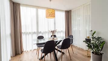 A dining area with a glass table, black chairs, a vase with flowers, and a hanging light fixture.