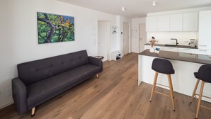 Un espace de vie moderne comprenant un canapé, un tableau, un coin cuisine avec des meubles blancs et un plancher en bois.