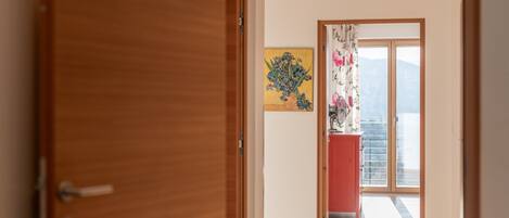 A hallway with a wooden door, a painting on the wall, and a view through a glass door to the outside.