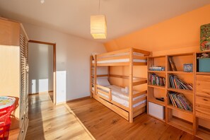 Una habitación con literas, una estantería y una puerta que da a otra habitación.
