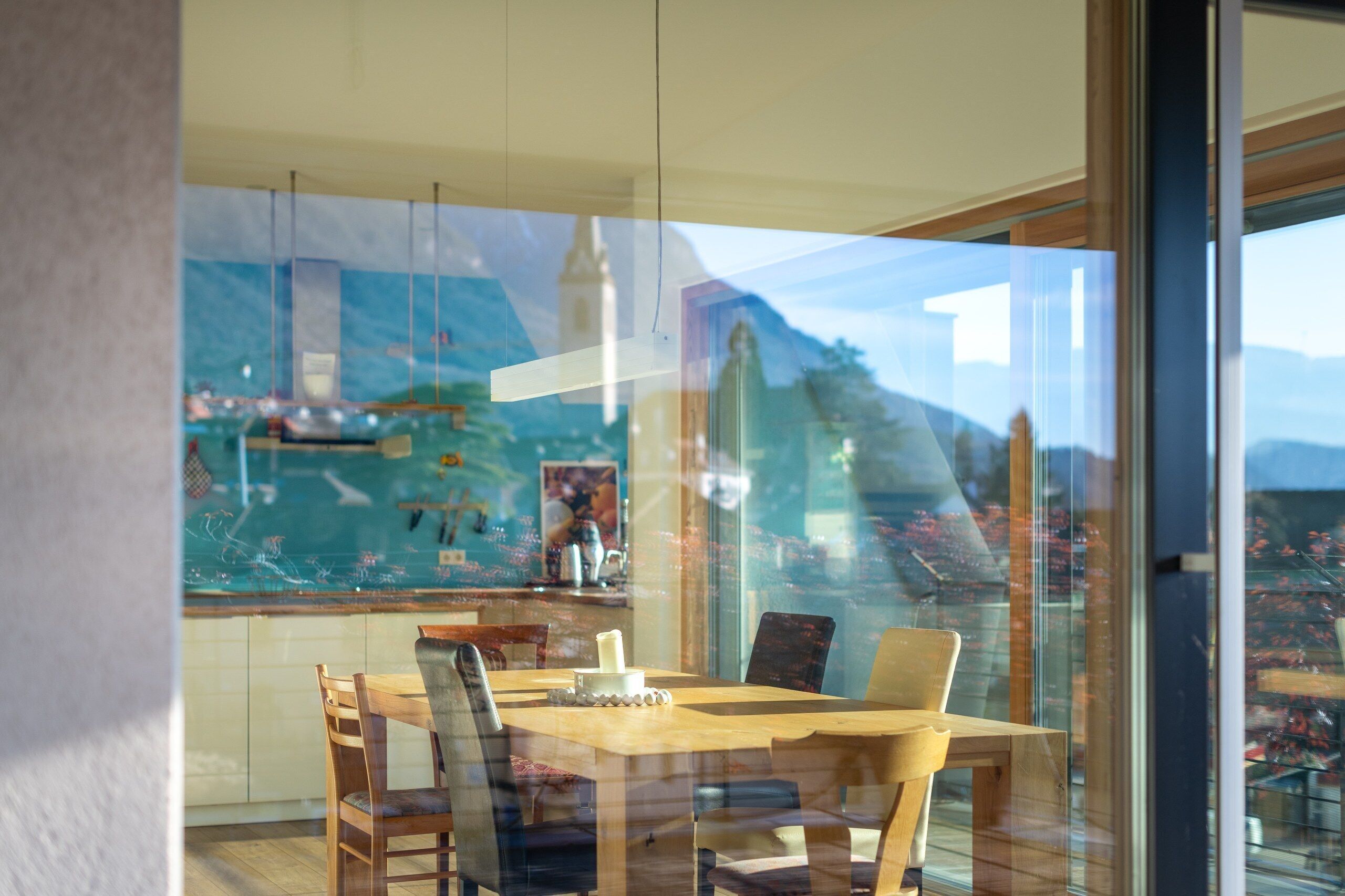 Un espace repas comprenant une table et des chaises en bois, une cloison en verre et une vue sur le paysage urbain et les montagnes, visibles à travers le verre.