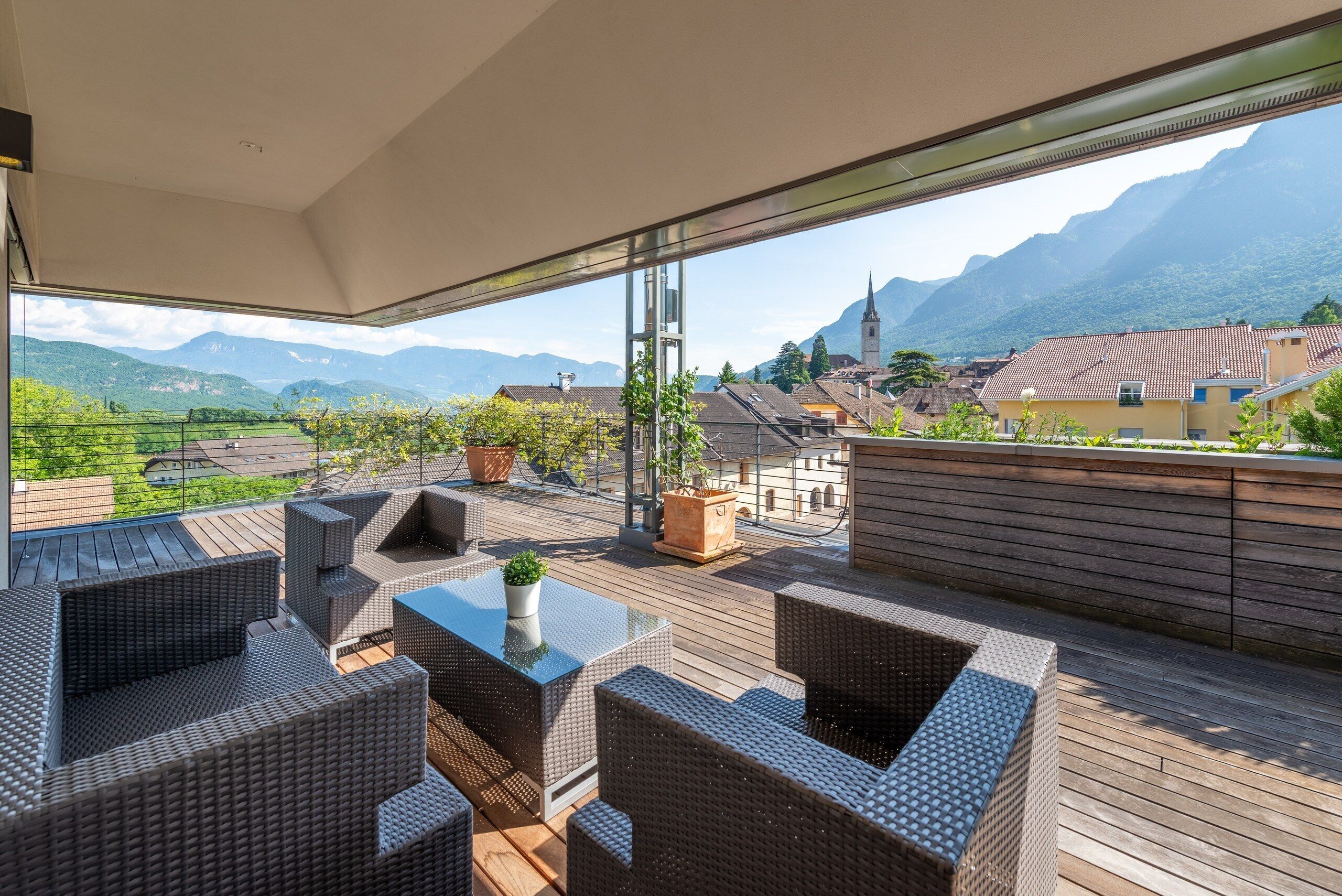 Une terrasse sur le toit, aménagée avec des meubles en osier, une table en verre et des plantes en pot.
