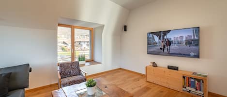 Una sala de estar moderna con piso de madera, un sofá, una mesa de centro, un televisor montado en la pared y una estantería.