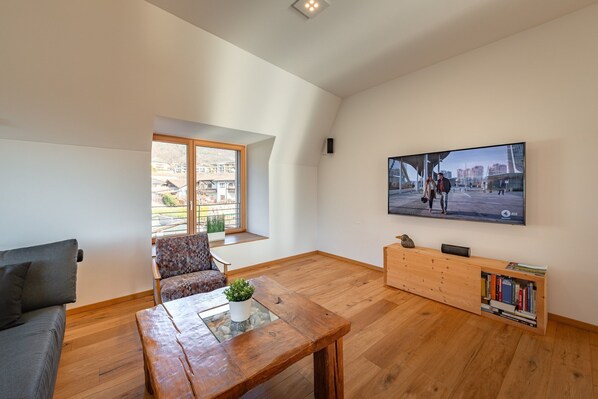 Una sala de estar moderna con piso de madera, un sofá, una mesa de centro, un televisor montado en la pared y una estantería.