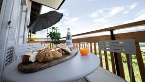 A table with a variety of breads and a bottle of water on a balcony with a wooden railing and a view of the sky.