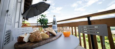Una mesa con panes variados y una botella de agua en un balcón con baranda de madera y vista al cielo.