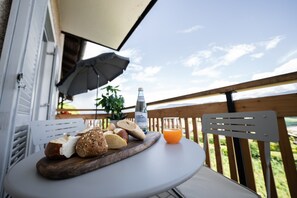 Une table sur laquelle sont disposés différents types de pain et une bouteille d’eau, sur un balcon doté d’une balustrade en bois et offrant une vue sur le ciel.