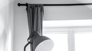 A room with a bed, a window with curtains, and a floor lamp.