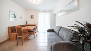 Una sala de estar moderna con comedor, un sofá gris, una mesa de comedor de madera con sillas y una planta grande.