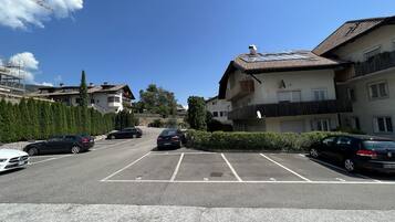 Un parking rempli de voitures, un immeuble doté de balcons et un ciel dégagé.