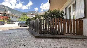 Un camino pavimentado con cerca de madera, autos estacionados y un edificio con fachada blanca.