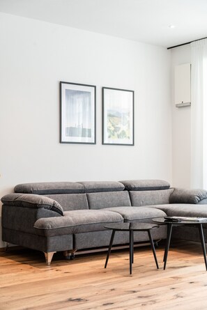 A modern living room with a grey sectional sofa, a small round table, and two framed artworks on the wall.