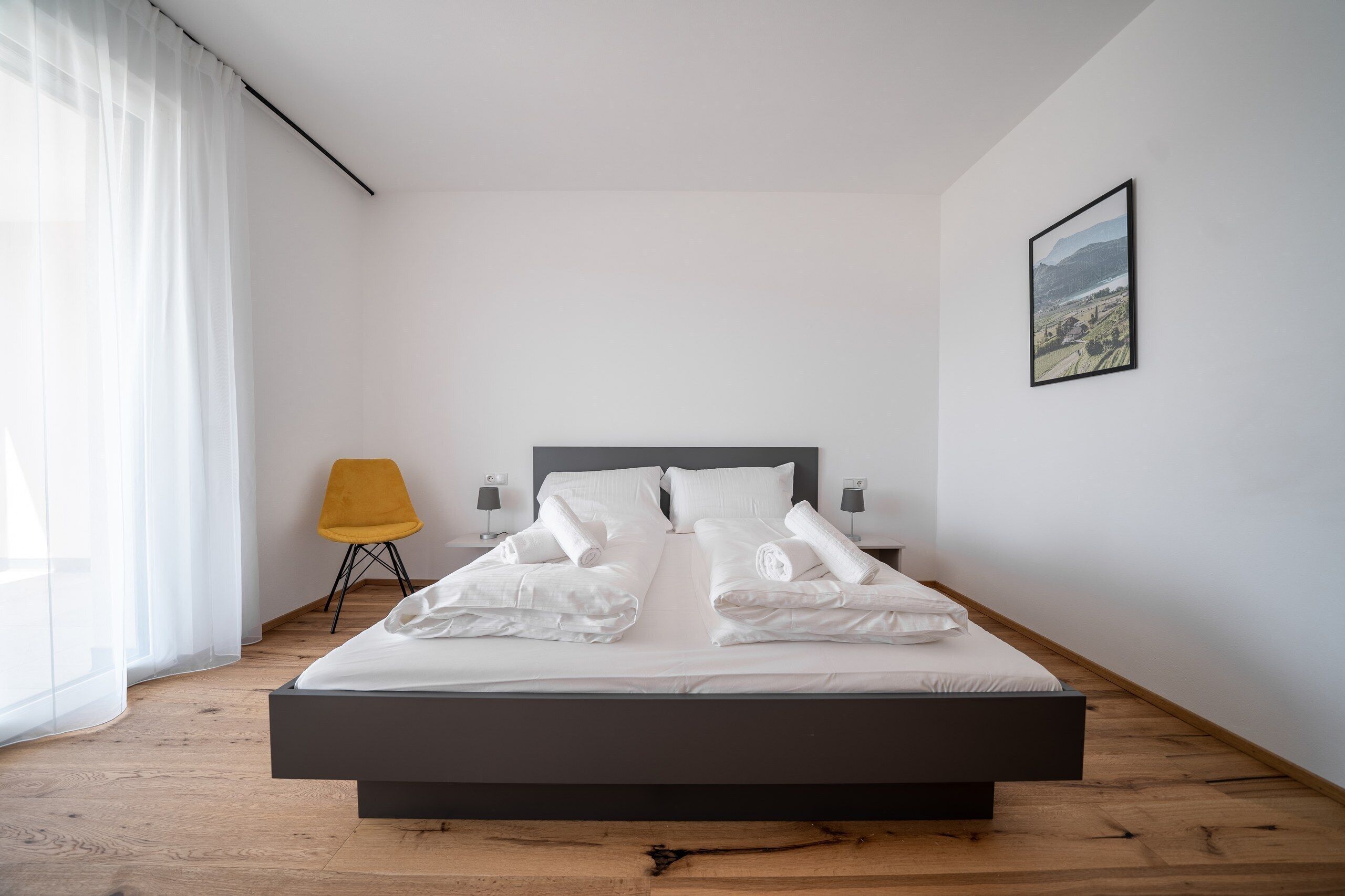 A modern bedroom with a large bed, a chair, and a painting on the wall.