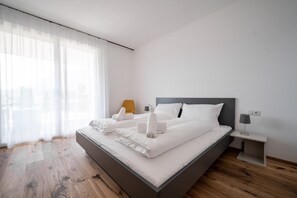 Un dormitorio moderno con una cama grande, una mesita de noche, una lámpara y una ventana con cortinas translúcidas.