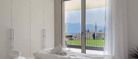 Une chambre d’hôtel avec une grande fenêtre, un lit avec du linge de maison blanc et une vue sur une ville et des montagnes.