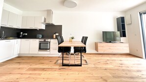 A modern kitchen with white cabinets, a wooden dining table, and a TV on a wooden stand.