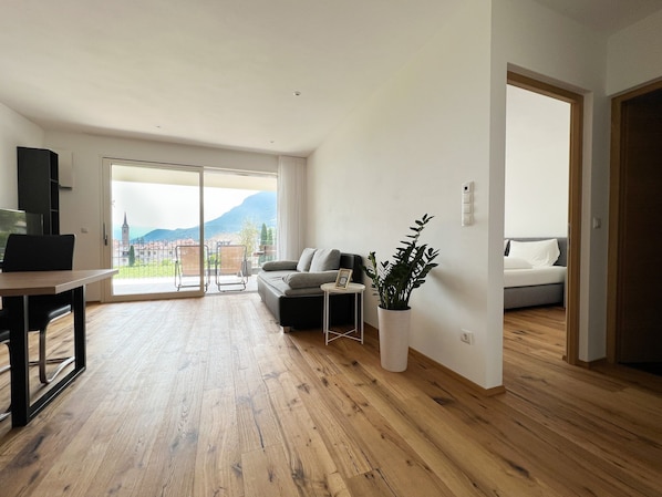 Un amplio espacio de sala con piso de madera, un sofá, una mesa de comedor y una planta en maceta.