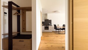 A modern interior with a wooden floor, a kitchenette, a dining area with a table and chairs, and a wardrobe with a hanging rack.