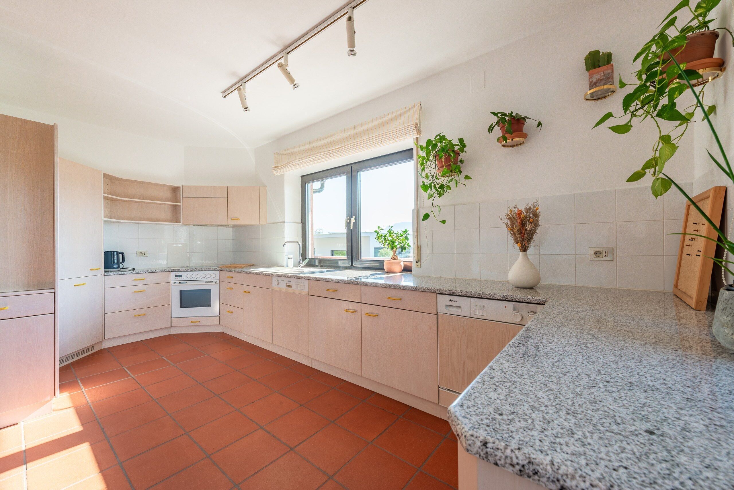 Una cocina moderna con armarios de madera clara, horno empotrado y encimera de granito.
