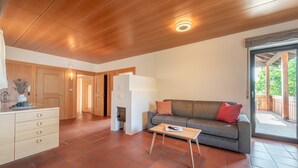 Un espacio habitable moderno con techo de madera, un sofá gris con cojines rojos, una pequeña mesa de centro de madera y un mueble blanco con cajones.