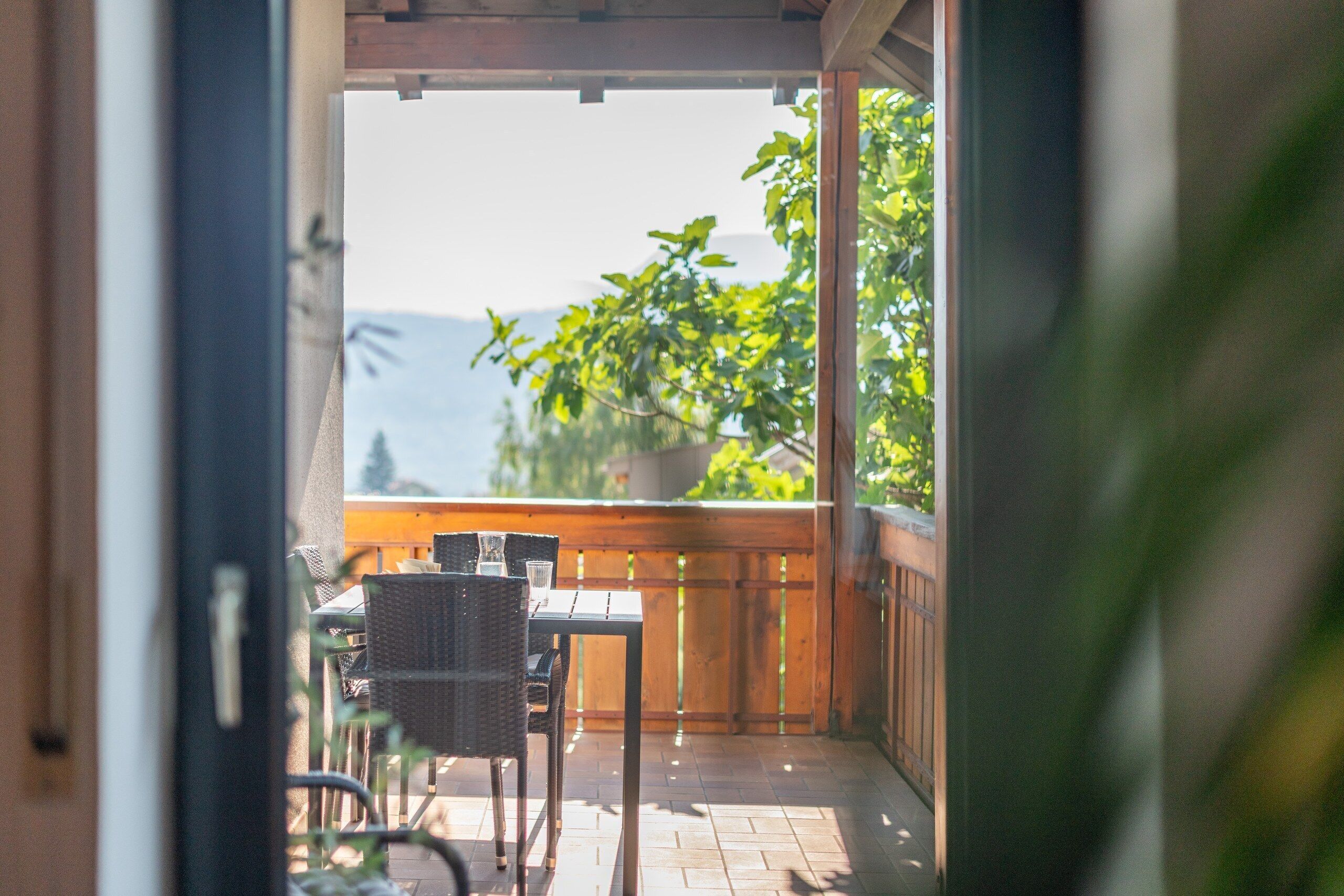 Un balcon avec une table et des chaises, un pot de fleurs et une vue sur la verdure et les montagnes.
