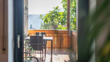 Un balcon avec une table et des chaises, un pot de fleurs et une vue sur la verdure et les montagnes.