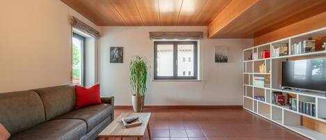 A living room with a sofa, a coffee table, a plant, a TV, and a bookshelf.