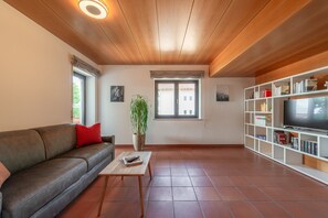 Una sala de estar con un sofá, una mesa de centro, una planta, un televisor y una estantería.