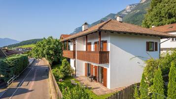 Une maison à deux étages avec un balcon, une allée pavée et une vue sur les montagnes en arrière-plan.