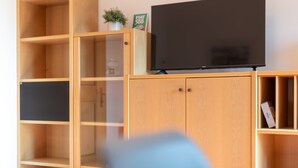 Ein Holz-Multifunktionsmöbel mit einem Flachbildfernseher darauf, einer kleinen Topfpflanze und einer Kiste mit dem Aufdruck 'FIAT'.