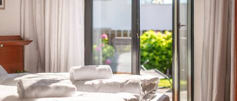 Habitación de hotel con cama, cabecera de madera, ventana con cortinas y vista a zonas verdes.