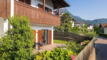 Una casa de dos pisos con un balcón, un patio de piedra y una cerca de madera.