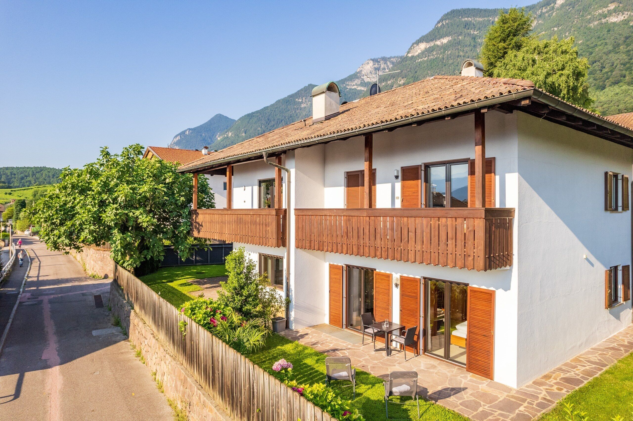 Ein zweistöckiges Haus mit Balkon, einer Steinterrasse und Blick auf Berge.