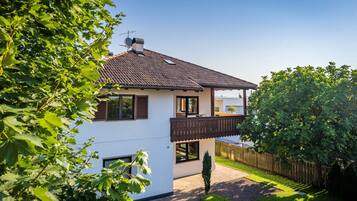 Een huis met twee verdiepingen, een pannendak, een balkon en een omheinde tuin.