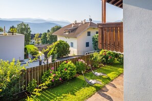 A residential property with a well-maintained garden, a patio with a lounge chair, and a view of distant mountains. - 714A Apartment Villa Vardia (Caldaro sulla strada del vino)
