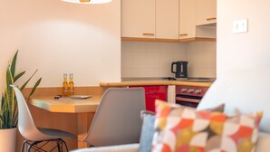 Eine moderne Küche mit weißen Schränken, einer Holz Arbeitsplatte, einer Kaffeemaschine und einem roten Gerät. Auf der Arbeitsplatte stehen zwei Flaschen, ein Topf mit Pflanze und ein Stuhl mit Sitzkissen.