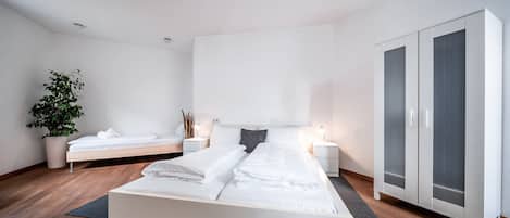 Une chambre moderne avec un grand lit, un plus petit lit, une armoire et une plante en pot.