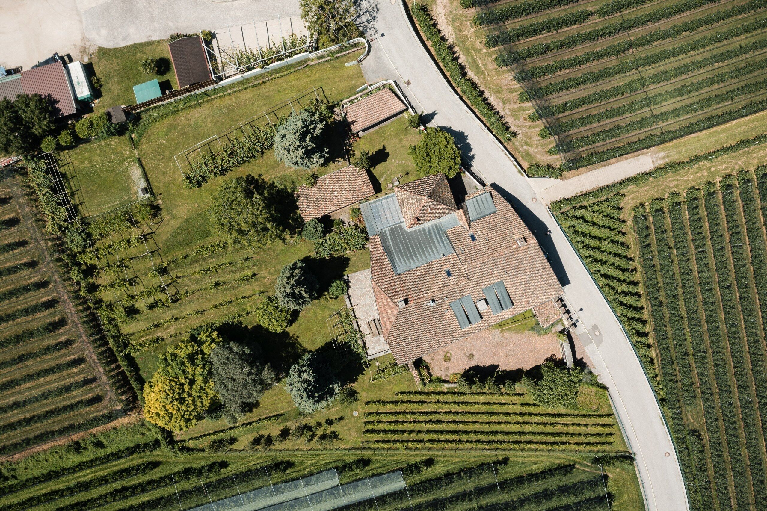 Vue aérienne d’une propriété dont le bâtiment principal est entouré de jardins aménagés et de rangées de vignes.